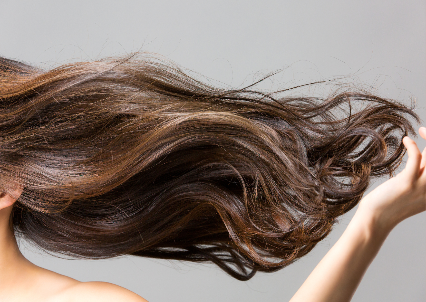 A fotografia mostra em destaque um cabelo castanho ao vento, lisos e com um braço de mulher branca aparecendo parcialmente.